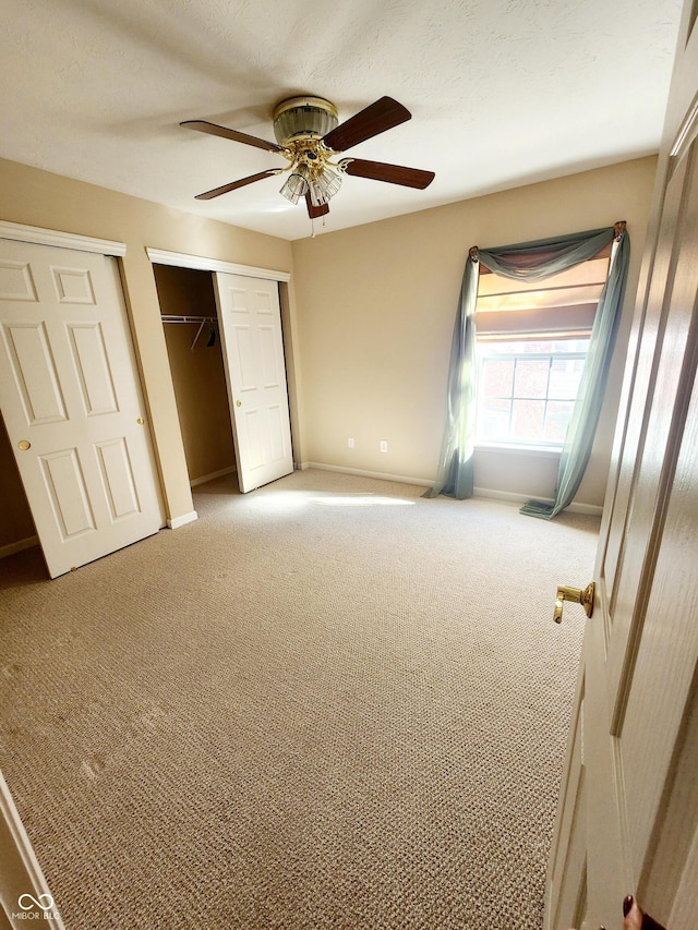 unfurnished bedroom featuring carpet flooring, two closets, and ceiling fan