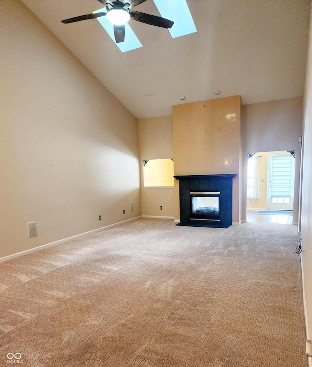 unfurnished living room featuring high vaulted ceiling, a skylight, a tile fireplace, and carpet flooring