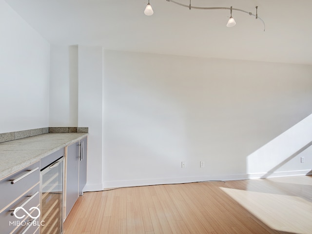 bar featuring light stone counters, beverage cooler, and light wood-type flooring