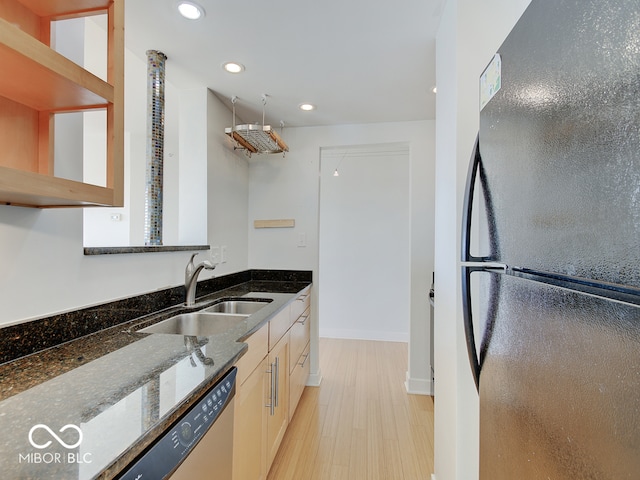 kitchen featuring sink, light hardwood / wood-style flooring, stainless steel dishwasher, dark stone countertops, and black refrigerator