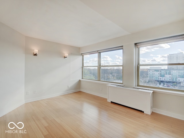 spare room with radiator, a healthy amount of sunlight, and light wood-type flooring