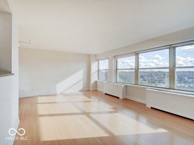 empty room with radiator heating unit, a wealth of natural light, and light hardwood / wood-style flooring