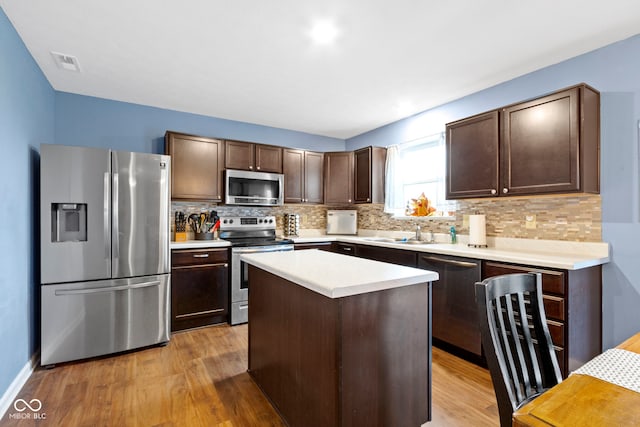 kitchen with a center island, tasteful backsplash, dark brown cabinets, light hardwood / wood-style floors, and stainless steel appliances