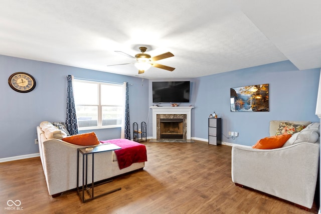 living room featuring hardwood / wood-style flooring, ceiling fan, a premium fireplace, and a textured ceiling