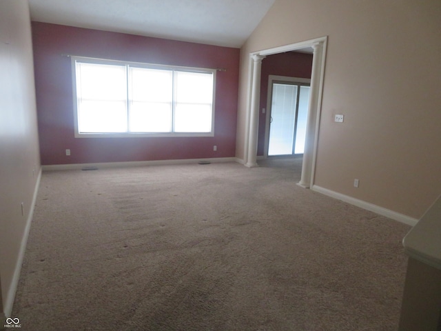 carpeted spare room featuring ornate columns and lofted ceiling