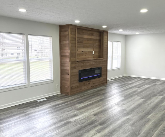 unfurnished living room with a textured ceiling, dark hardwood / wood-style flooring, and a large fireplace