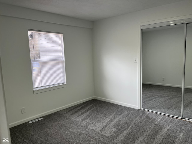 unfurnished bedroom featuring dark carpet and a closet