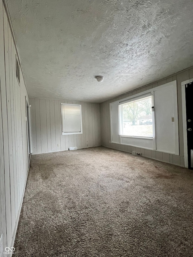 empty room with carpet flooring, wood walls, and a textured ceiling