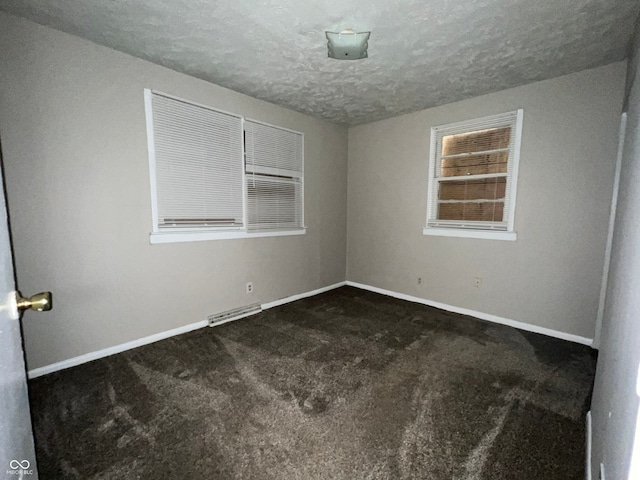 empty room with dark carpet and a textured ceiling