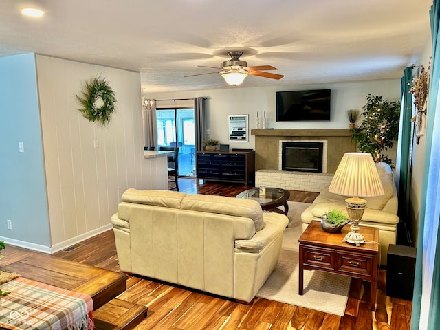 living room with wood-type flooring, ceiling fan with notable chandelier, and a brick fireplace