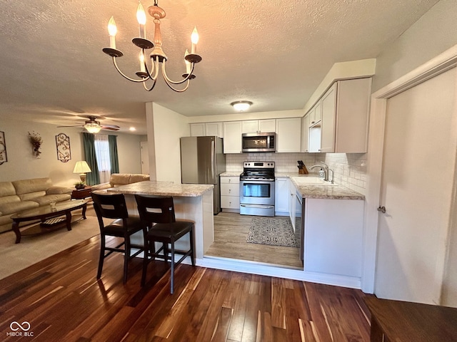 kitchen with dark hardwood / wood-style floors, a textured ceiling, decorative light fixtures, white cabinets, and appliances with stainless steel finishes
