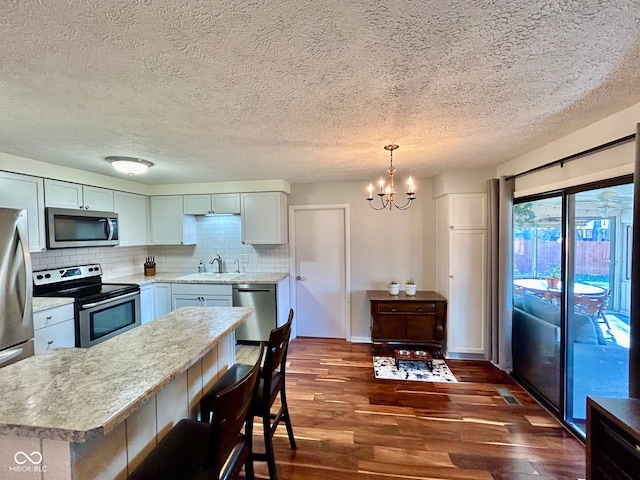 kitchen with pendant lighting, dark wood-type flooring, sink, appliances with stainless steel finishes, and a chandelier