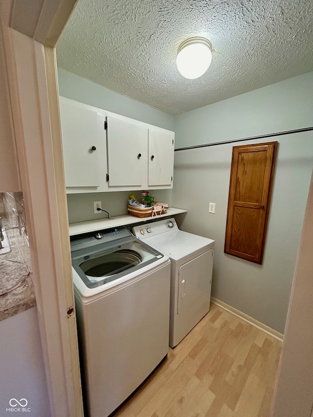 washroom featuring cabinets, light hardwood / wood-style floors, a textured ceiling, and independent washer and dryer