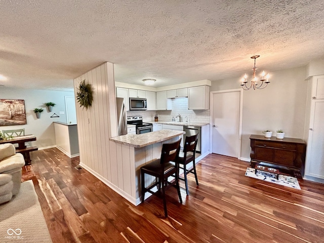 kitchen featuring sink, dark hardwood / wood-style floors, a textured ceiling, a breakfast bar area, and appliances with stainless steel finishes