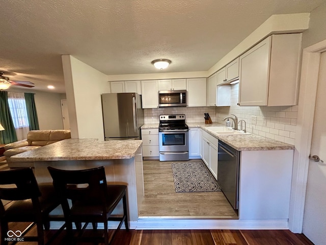 kitchen with white cabinetry, sink, dark wood-type flooring, a breakfast bar area, and appliances with stainless steel finishes