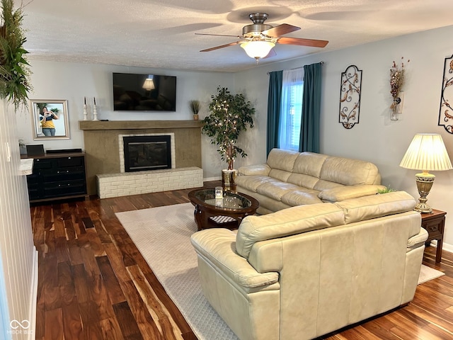 living room featuring a textured ceiling, dark hardwood / wood-style flooring, a brick fireplace, and ceiling fan