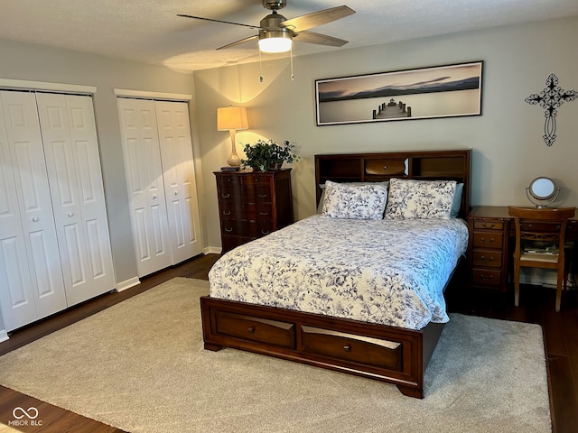bedroom featuring a textured ceiling, ceiling fan, two closets, and hardwood / wood-style flooring