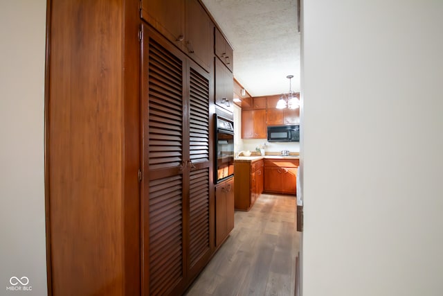 kitchen with a textured ceiling, black appliances, a chandelier, hardwood / wood-style floors, and hanging light fixtures