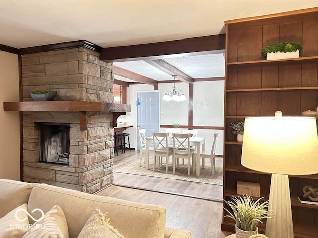 living room with beam ceiling, an inviting chandelier, light hardwood / wood-style floors, and a stone fireplace