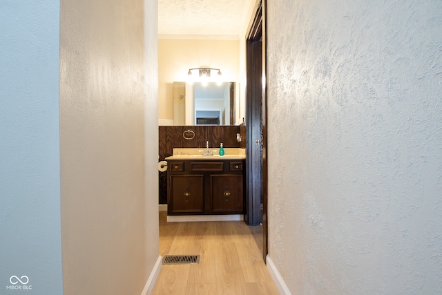 hall with a textured ceiling, light hardwood / wood-style floors, ornamental molding, and sink