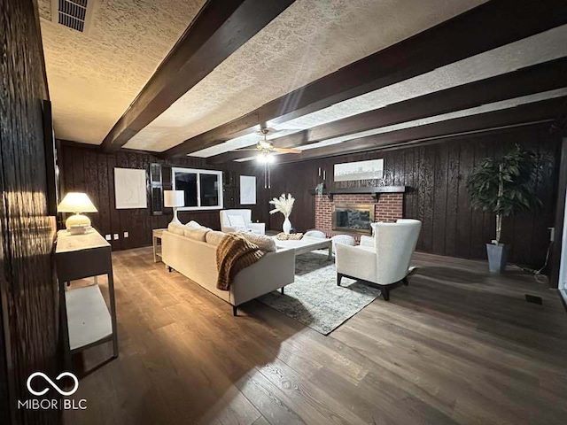 living room featuring a fireplace, a textured ceiling, ceiling fan, wood-type flooring, and beamed ceiling