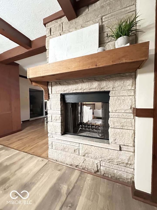 interior details featuring beamed ceiling, wood-type flooring, a fireplace, and a textured ceiling