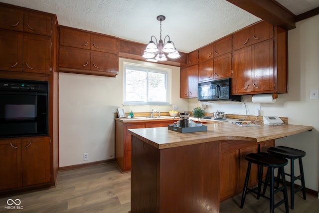 kitchen with hanging light fixtures, kitchen peninsula, a textured ceiling, black appliances, and light wood-type flooring