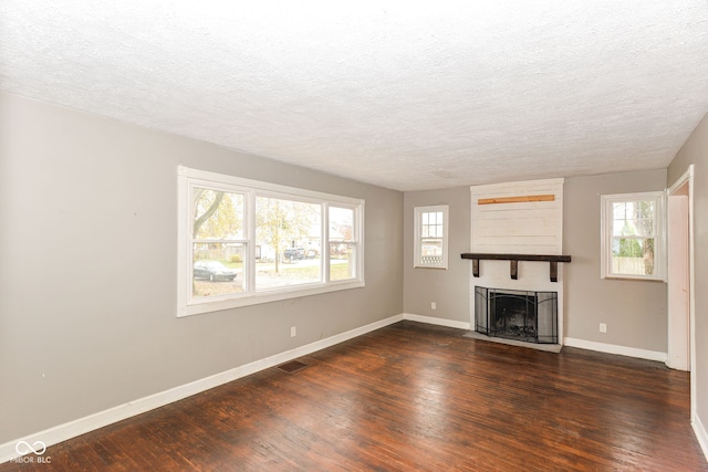 unfurnished living room featuring a large fireplace, plenty of natural light, a textured ceiling, and dark hardwood / wood-style floors