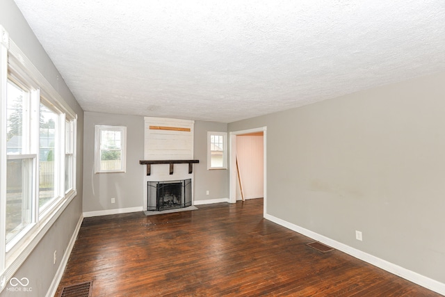 unfurnished living room featuring a fireplace, a textured ceiling, and dark wood-type flooring