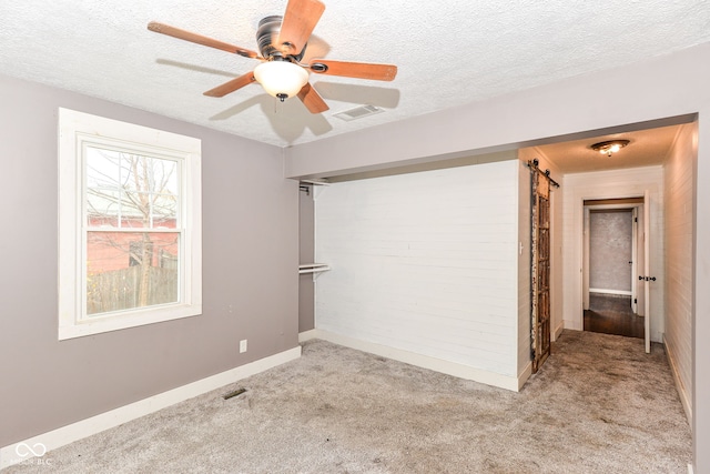 carpeted spare room with ceiling fan, a barn door, and a textured ceiling