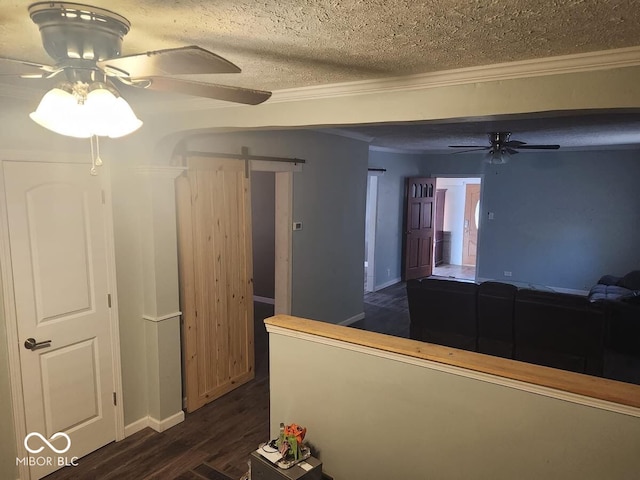 corridor with a textured ceiling, a barn door, dark hardwood / wood-style floors, and ornamental molding