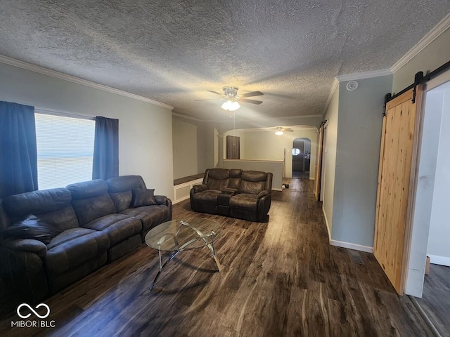 living room with dark hardwood / wood-style floors, a barn door, ceiling fan, ornamental molding, and a textured ceiling