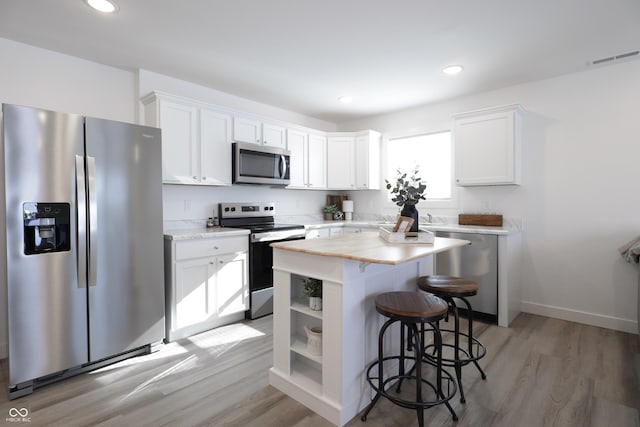 kitchen featuring stainless steel appliances, a center island, white cabinets, a kitchen bar, and light wood-type flooring