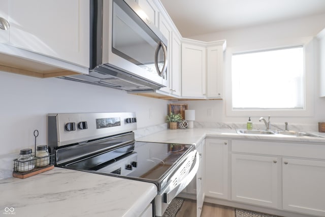 kitchen with sink, white cabinetry, light stone counters, appliances with stainless steel finishes, and light hardwood / wood-style floors