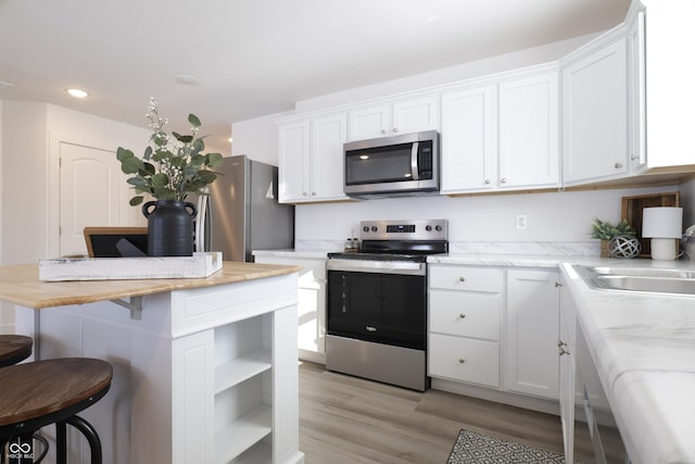 kitchen featuring sink, a breakfast bar, appliances with stainless steel finishes, white cabinets, and light wood-type flooring