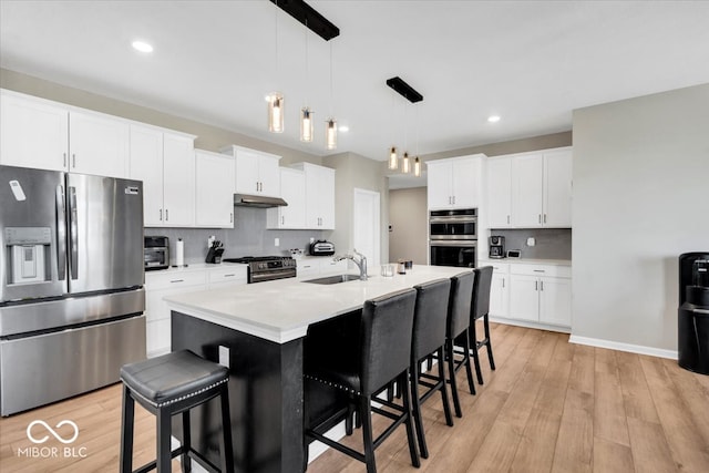 kitchen with sink, hanging light fixtures, stainless steel appliances, light hardwood / wood-style floors, and a kitchen island with sink