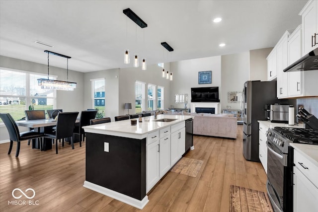 kitchen featuring an island with sink, light hardwood / wood-style floors, decorative light fixtures, and appliances with stainless steel finishes