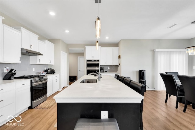 kitchen featuring light wood-type flooring, stainless steel appliances, a kitchen island with sink, and sink