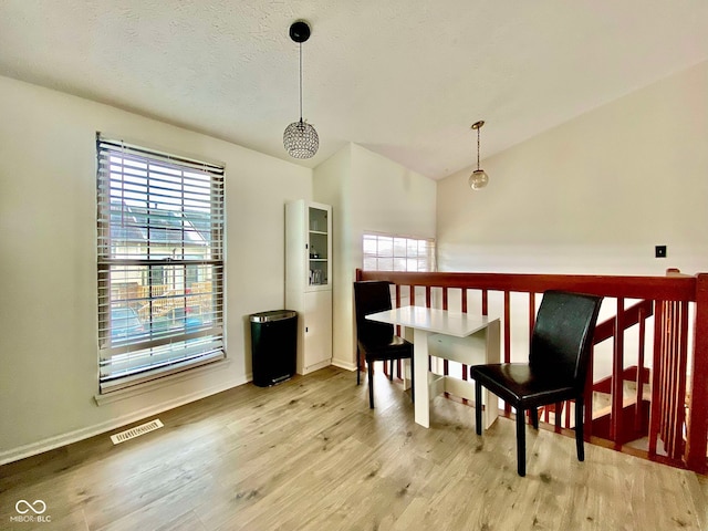 dining room featuring a textured ceiling, light hardwood / wood-style floors, and lofted ceiling