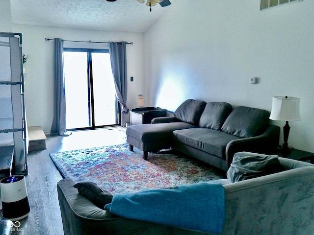 living room with hardwood / wood-style flooring, ceiling fan, a textured ceiling, and vaulted ceiling