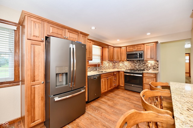 kitchen with appliances with stainless steel finishes, tasteful backsplash, light hardwood / wood-style flooring, and light stone counters