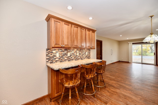 kitchen featuring light stone countertops, a kitchen bar, dark hardwood / wood-style flooring, backsplash, and hanging light fixtures