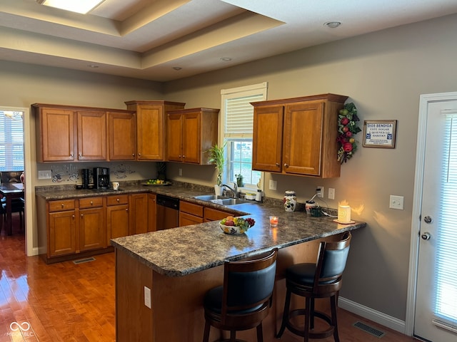 kitchen featuring dishwasher, sink, dark hardwood / wood-style flooring, kitchen peninsula, and a breakfast bar area