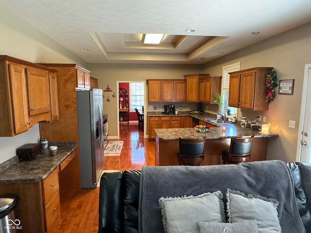 kitchen with sink, a raised ceiling, dark hardwood / wood-style flooring, kitchen peninsula, and stainless steel fridge