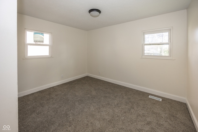 spare room featuring dark colored carpet and a healthy amount of sunlight