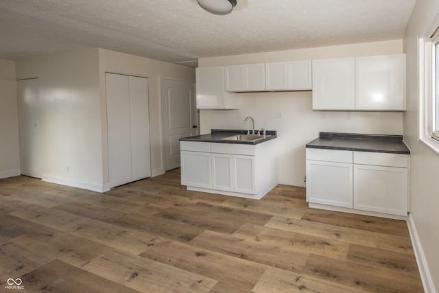 kitchen with a textured ceiling, light wood-type flooring, white cabinetry, and sink