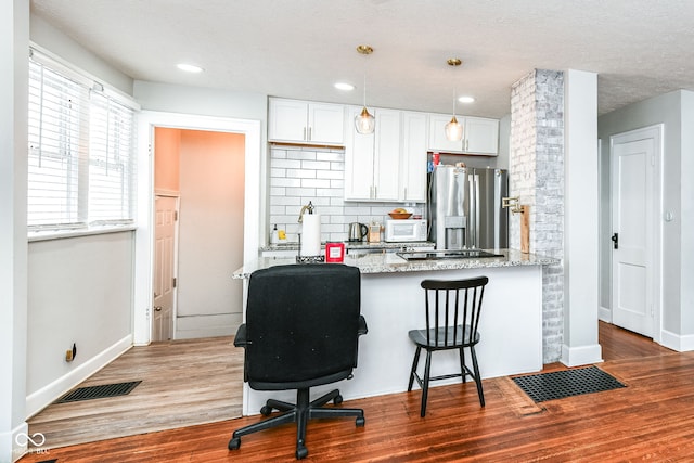 kitchen with white cabinetry, stainless steel fridge, hardwood / wood-style floors, and hanging light fixtures