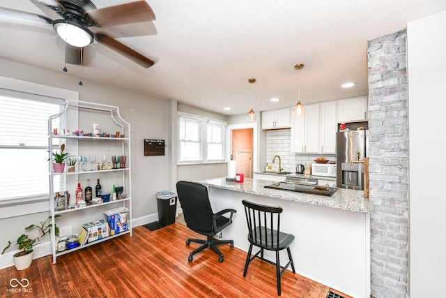 kitchen featuring white cabinets, stainless steel fridge, dark hardwood / wood-style flooring, light stone counters, and a breakfast bar area