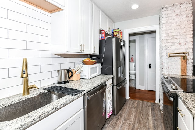 kitchen with light stone countertops, white cabinetry, dark wood-type flooring, stainless steel appliances, and a textured ceiling