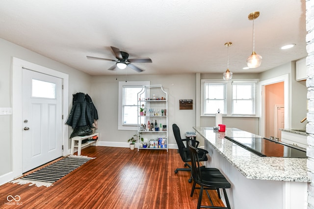 kitchen featuring dark hardwood / wood-style floors, light stone countertops, black electric cooktop, decorative light fixtures, and a kitchen bar